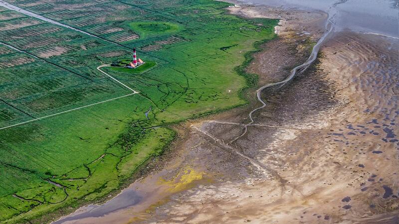 Areal picture of lighthouse set in lush green salt marhes next to exposed mudflat. Martin Stock/LKN.SH. Areal picture of lighthouse set in lush green salt marhes next to exposed mudflat. Martin Stock/LKN.SH.