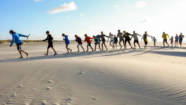 Group of children on sandy beach pulling a rope togehter. © Henk Postma.